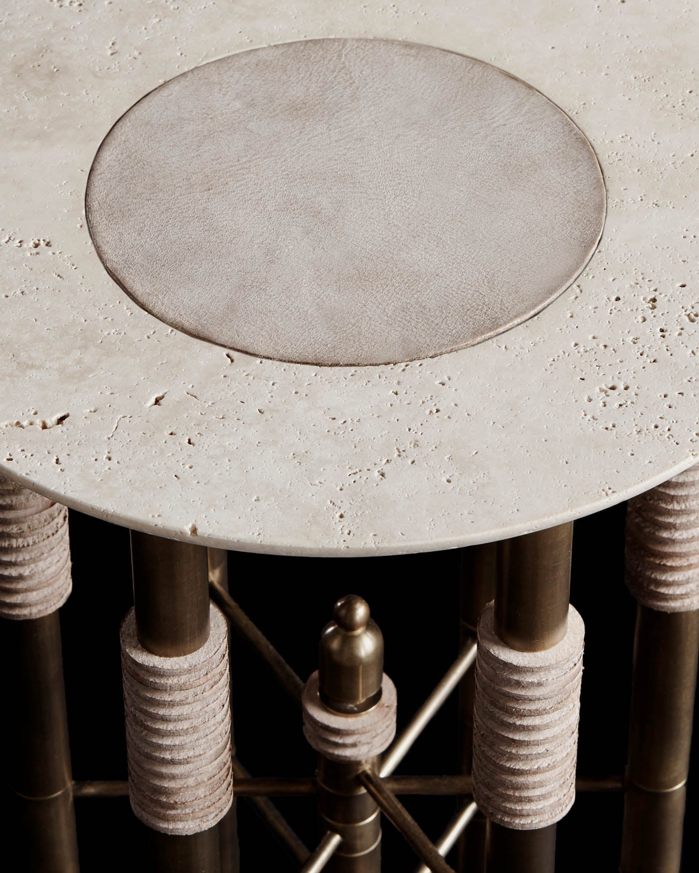 Close-up of a cocktail table with textured stone top and brass legs wrapped in light-colored rope against black background