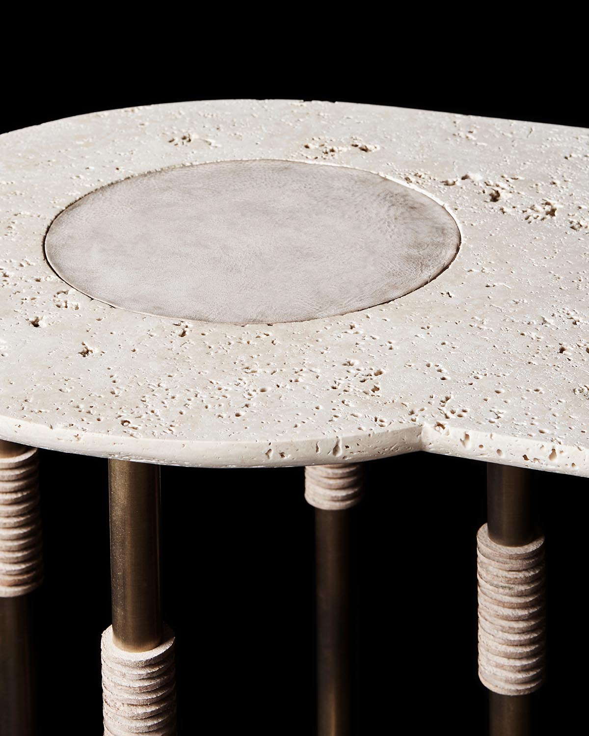 Close-up of beige stone console table top with circular inset and textured cylindrical legs against black background