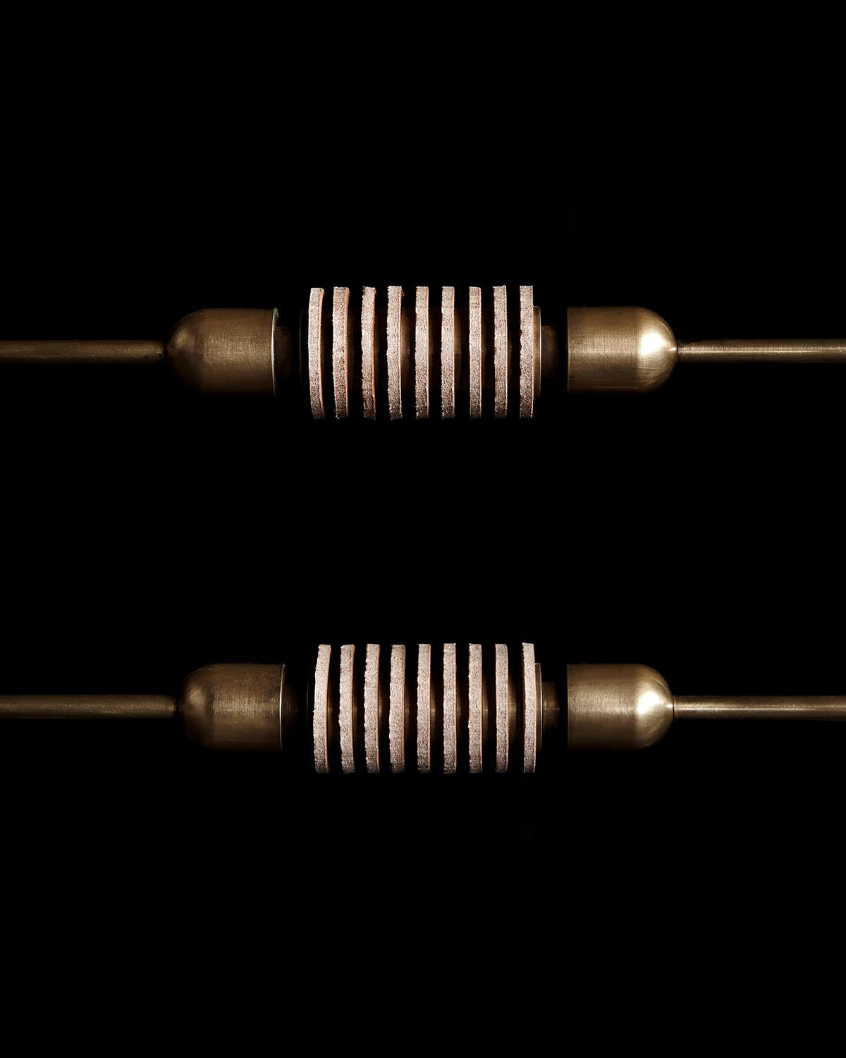 Close-up of two bronze cylindrical handles with evenly spaced ribbed bands against a black background