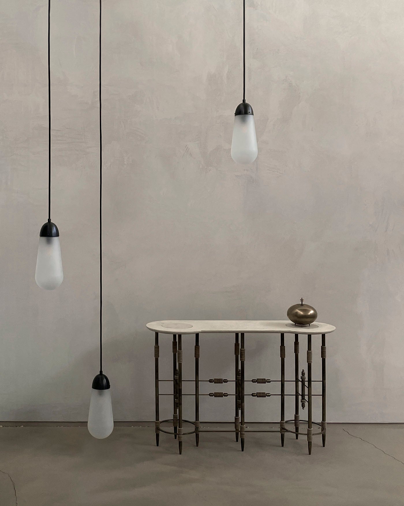 Oval marble console table with slender metal legs featuring decorative joints, against a textured neutral wall background