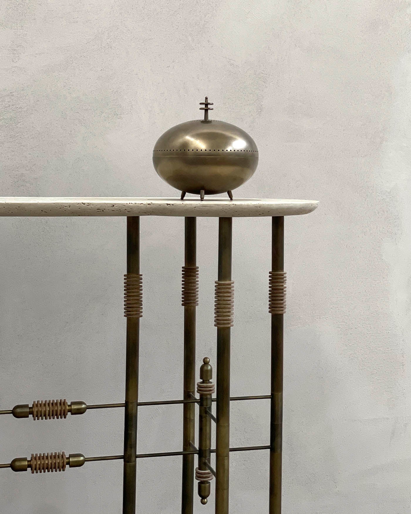 Close-up of console table corner with smooth light stone top and vertical bronze rods featuring spiral accents against a neutral wall