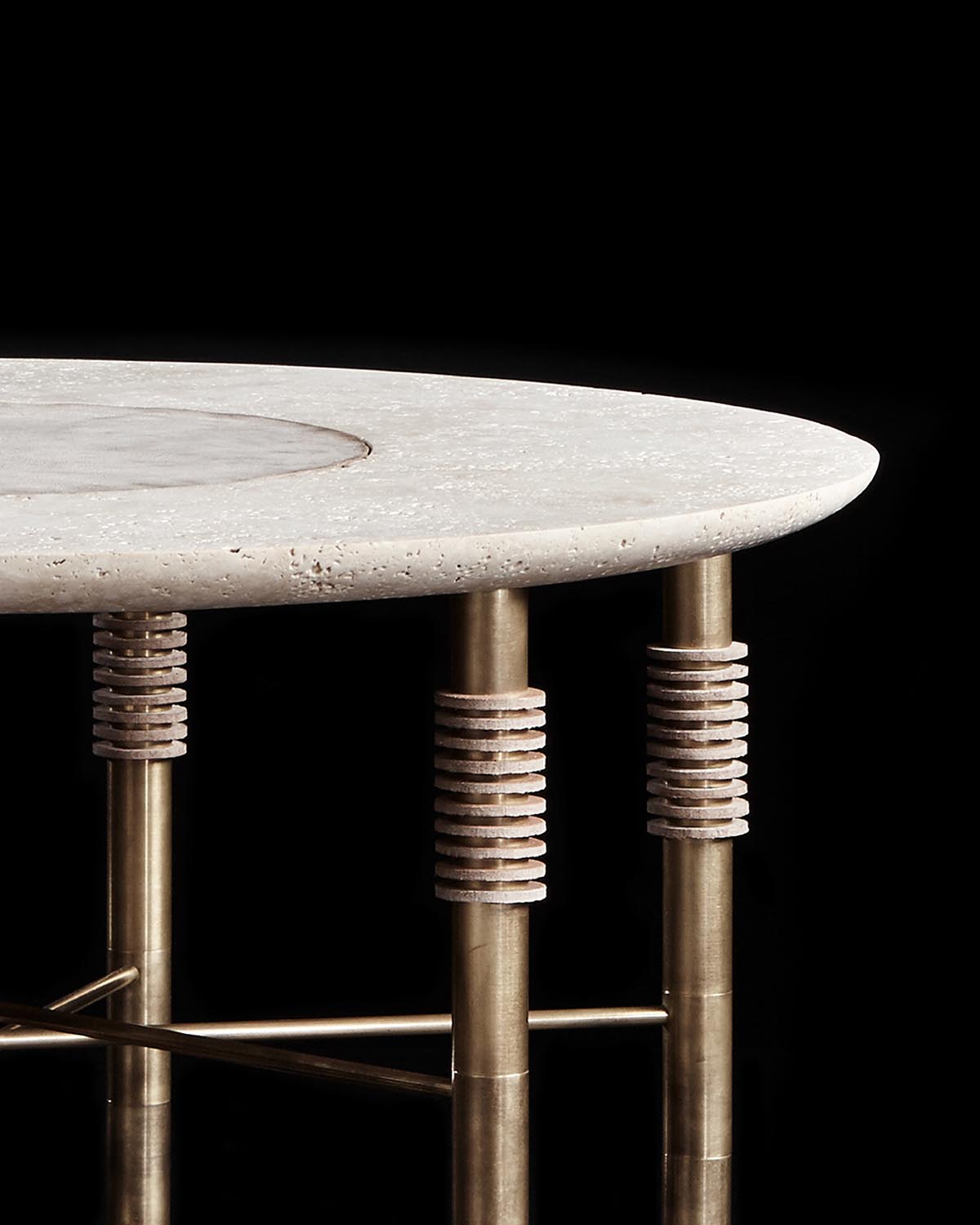 Close-up of round stone side table top with textured surface supported by brass legs featuring layered disc accents on black background