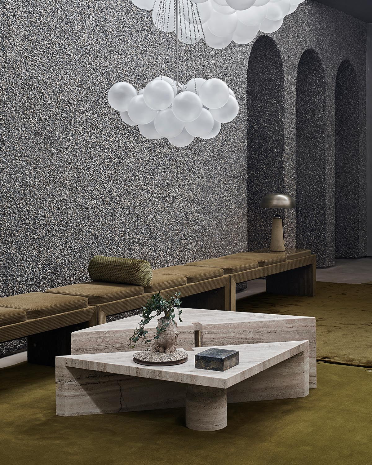 Geometric stone coffee table with textured top and cylindrical base in a modern room with arched wall niches and floating light fixture