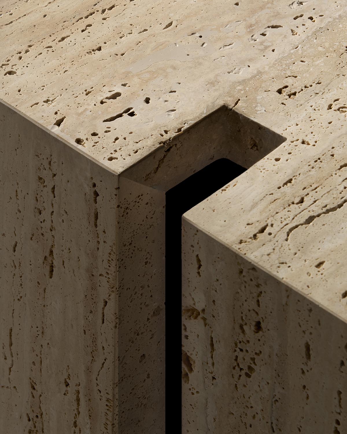 Close-up of a beige travertine console table corner with a recessed rectangular cutout and natural stone texture