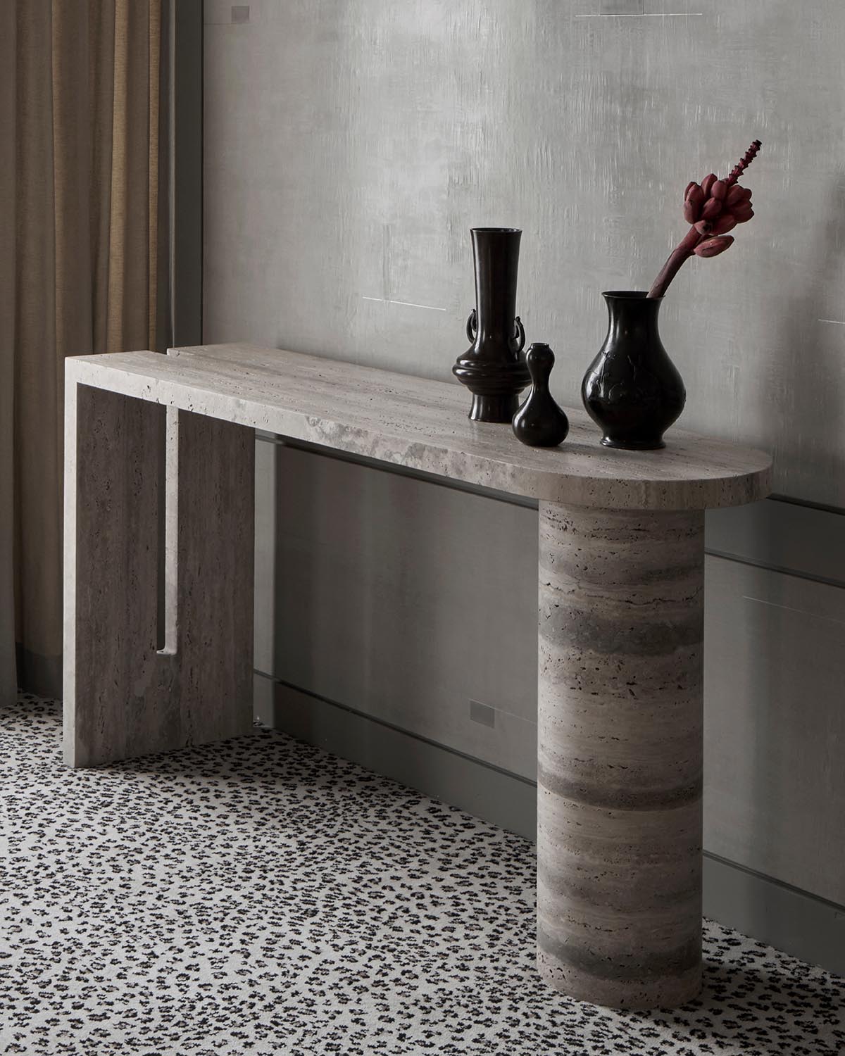 Minimalist console table in natural stone with contrasting rectangular and cylindrical legs and dark sculptural vases on top