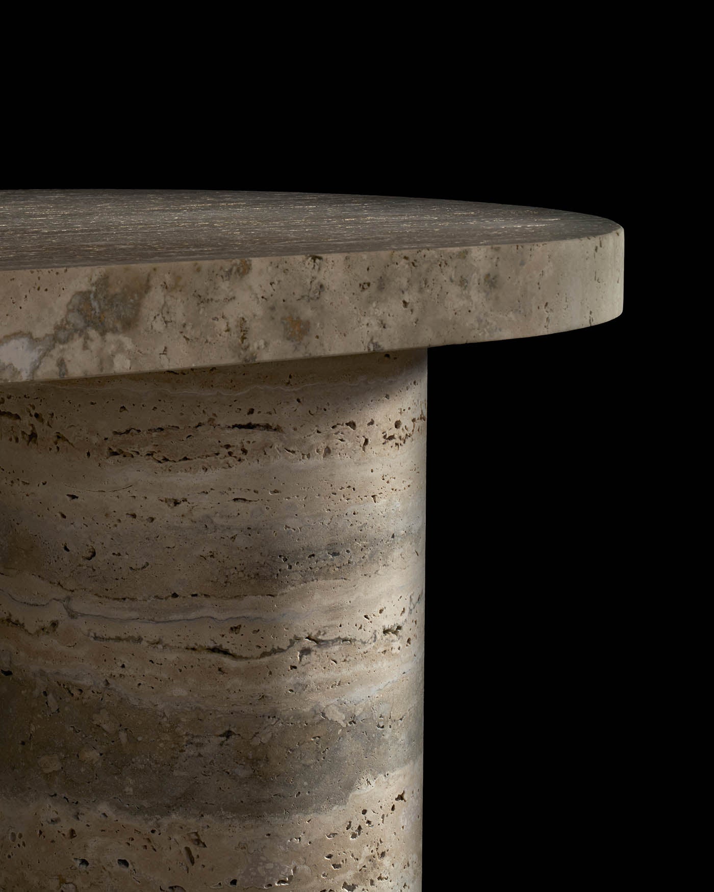 Close-up of a round console table with textured beige stone top and cylindrical base against a black background