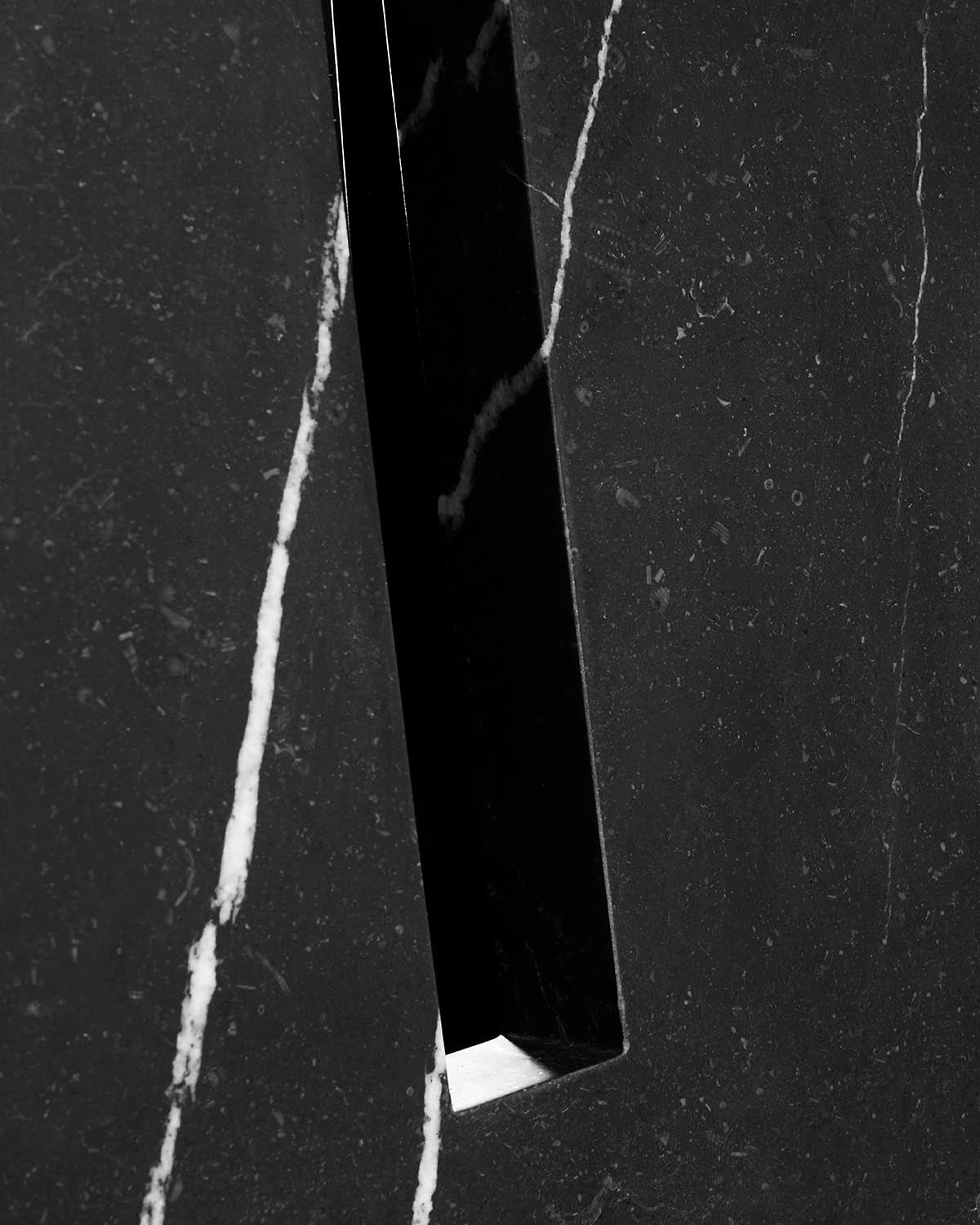 Close-up of black marble dining table surface with white veining and a narrow rectangular cutout detail
