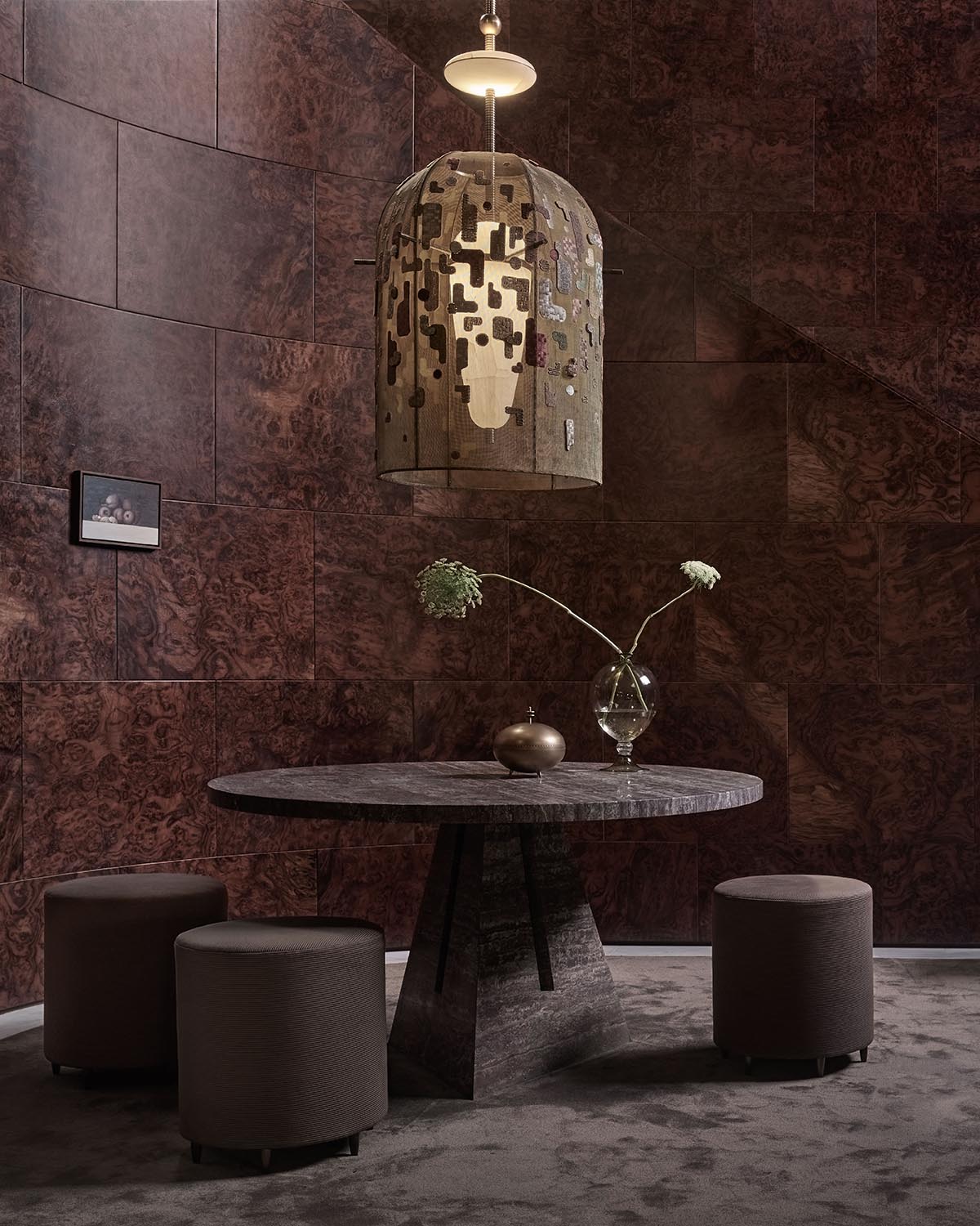 Round dark stone dining table with geometric pedestal base surrounded by three cylindrical brown stools in textured room