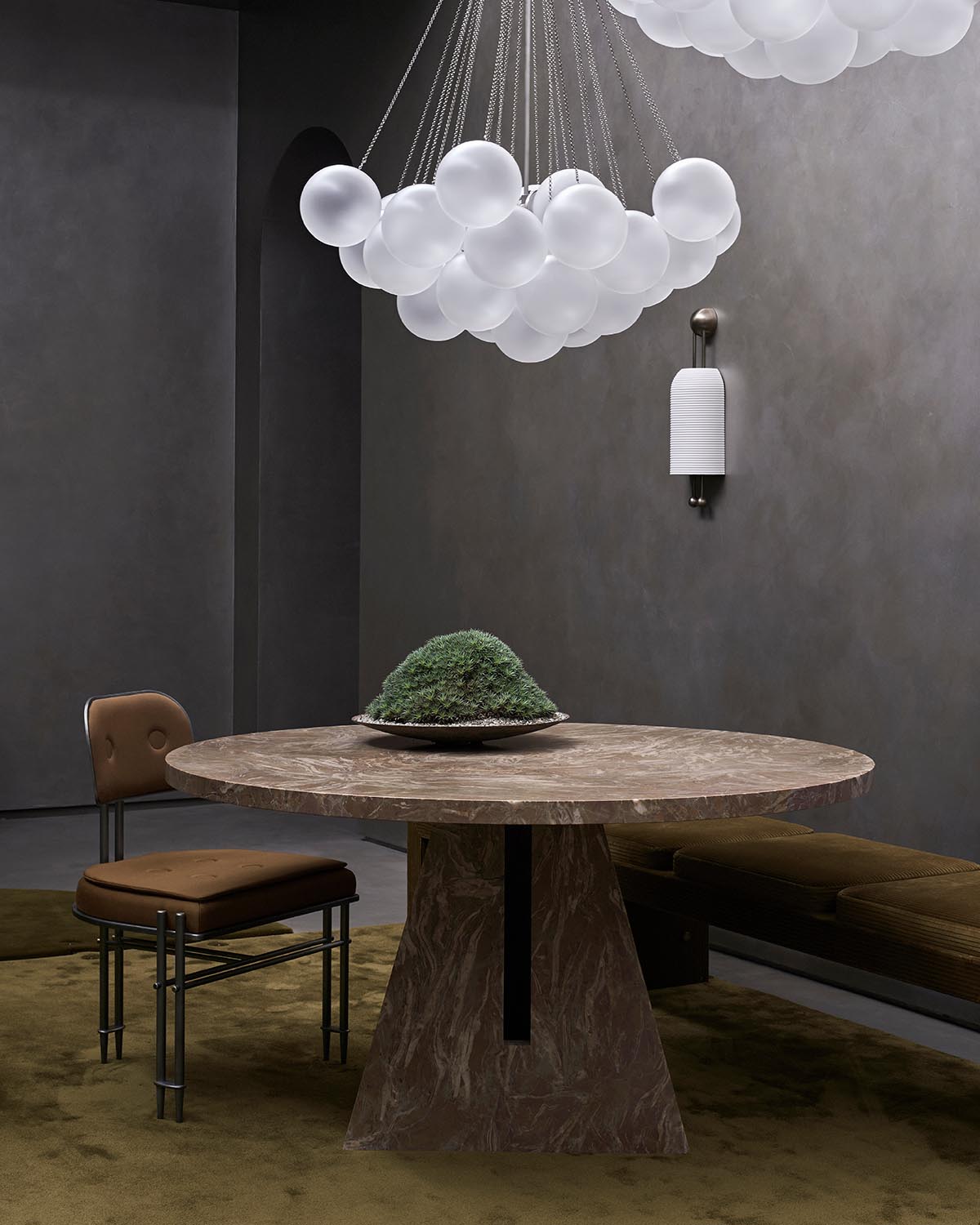 Round marble dining table with wide tapered base, surrounded by brown seating and modern pendant lights above