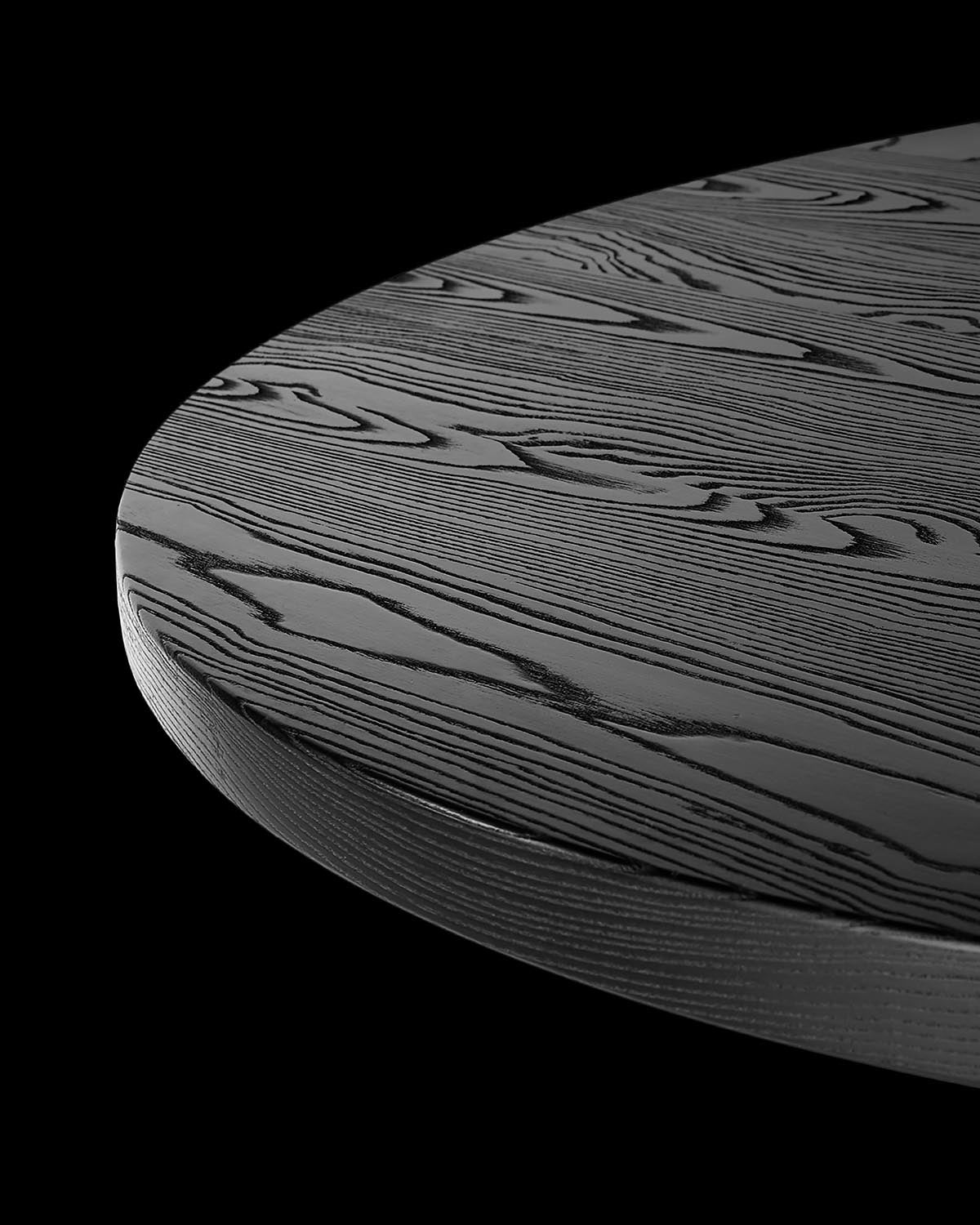 Close-up of round dining table top with textured dark wood grain pattern against a black background