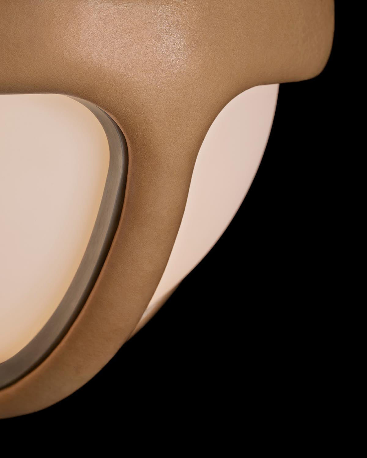 Close-up of a matte beige ceiling light fixture with smooth curved edges and a soft diffused glow on black background