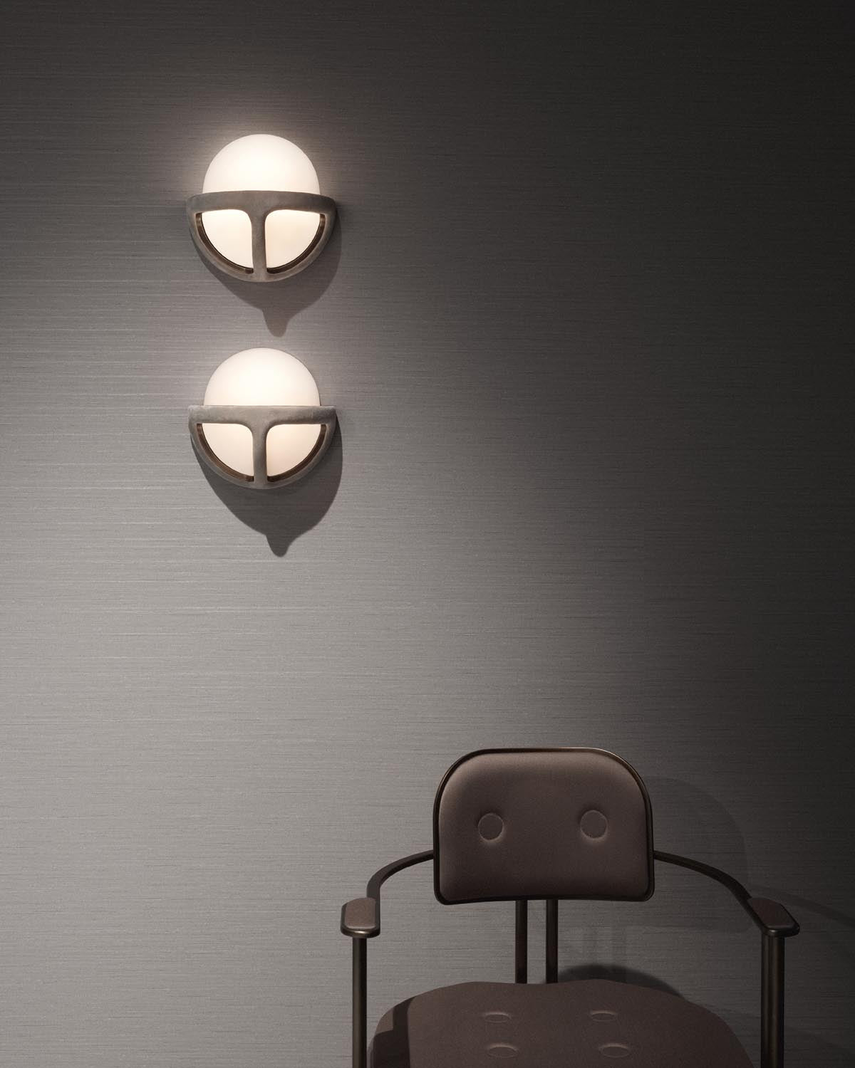 Two round white sconces with dark metal frames mounted on a textured gray wall above a dark cushioned chair