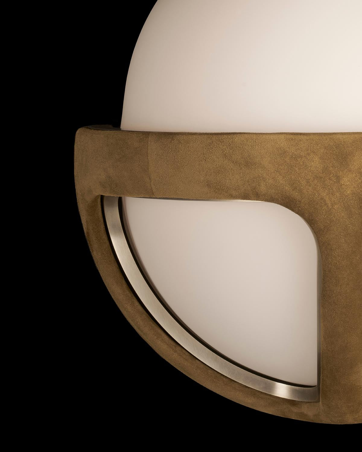 Close-up of a round white glass sconce with curved brass frame against a black background