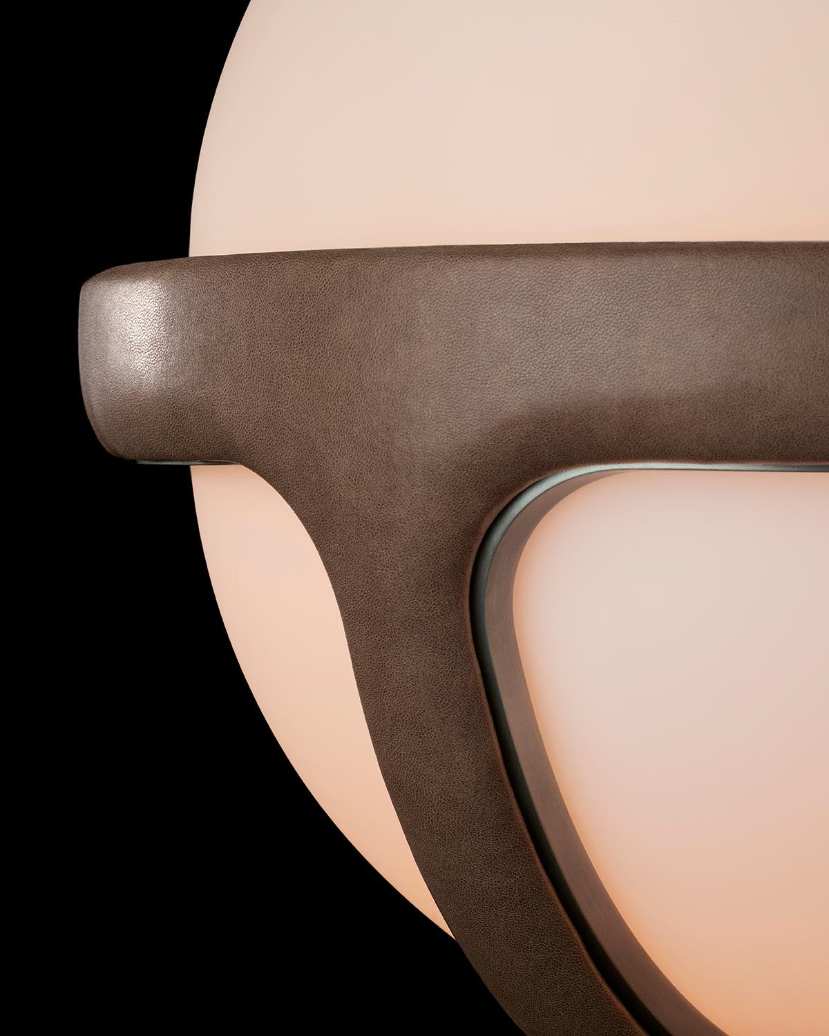 Close-up of a matte brown leather table lamp frame with soft glowing circular light against a black background