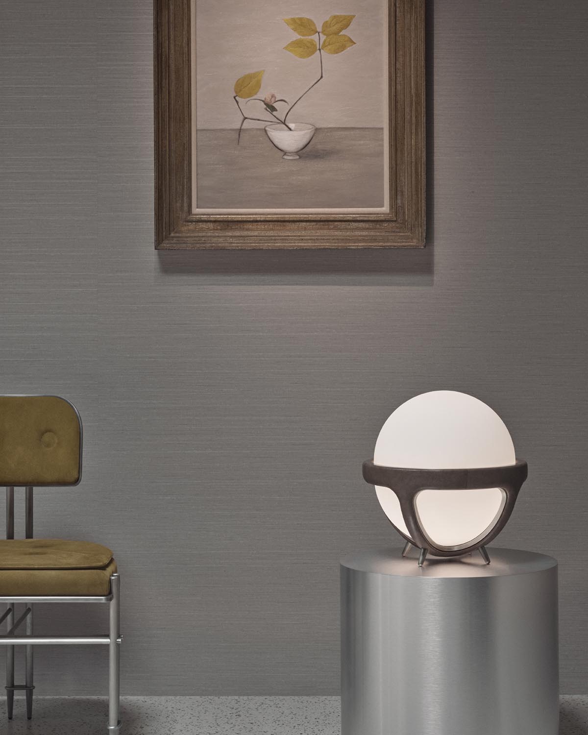 Minimalist interior featuring a round white table lamp with dark frame on a silver pedestal under framed botanical artwork