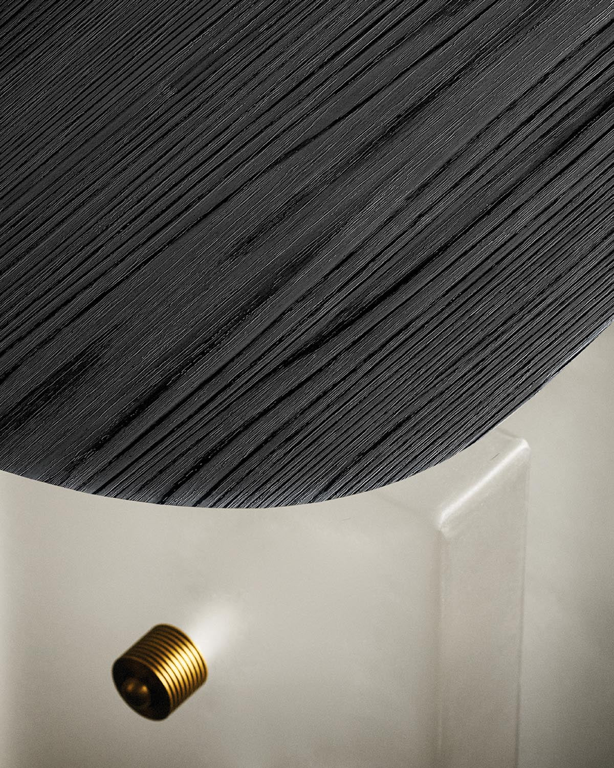 Close-up of a black textured wooden round tabletop with a brass detail on a translucent base against a neutral background