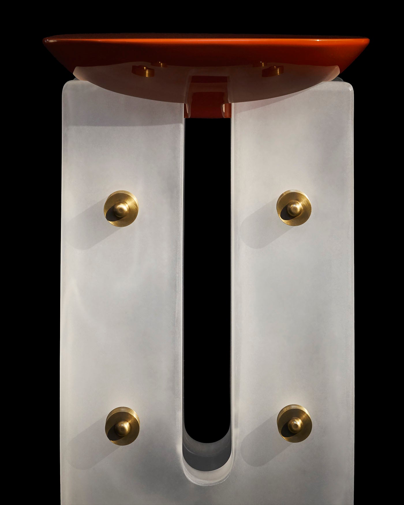 Close-up of a translucent white acrylic base with brass fittings supporting a glossy orange round tabletop against black background