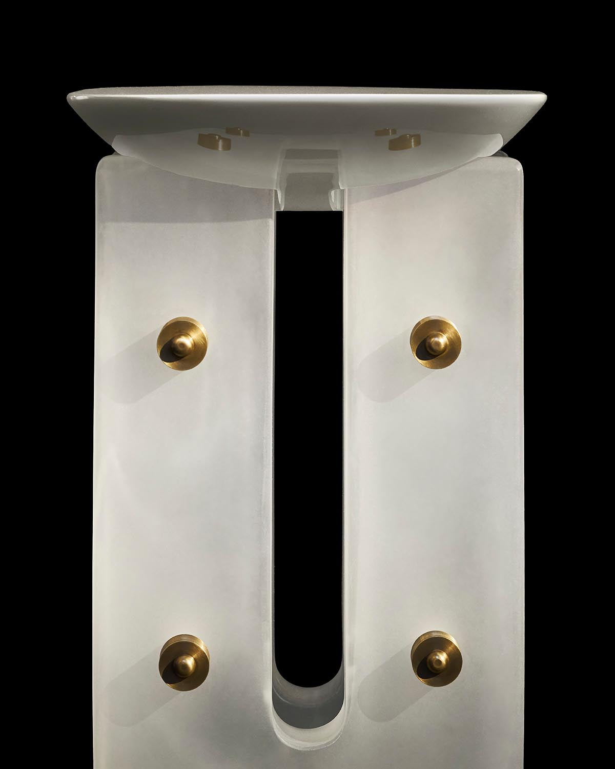 Modern ivory cocktail table base with four brass knobs and a flat top against black background