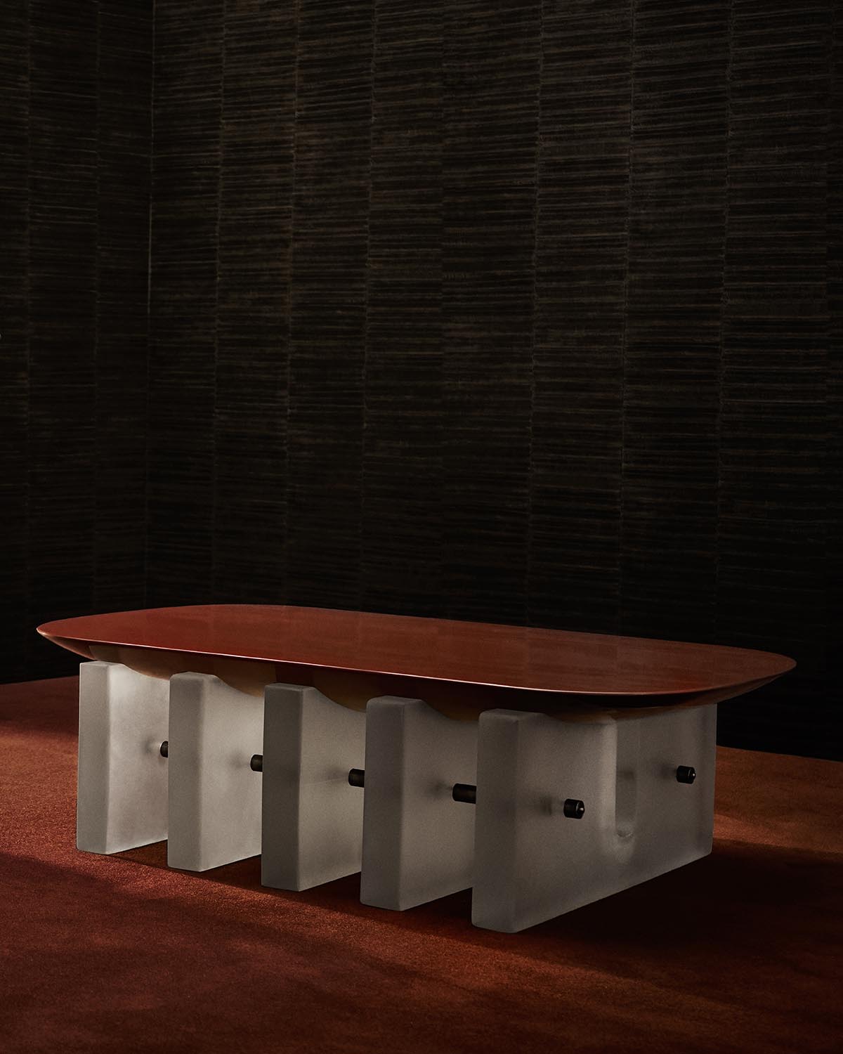 Rectangular coffee table with a smooth reddish wooden top and chunky translucent, sculptural base on a brown carpet