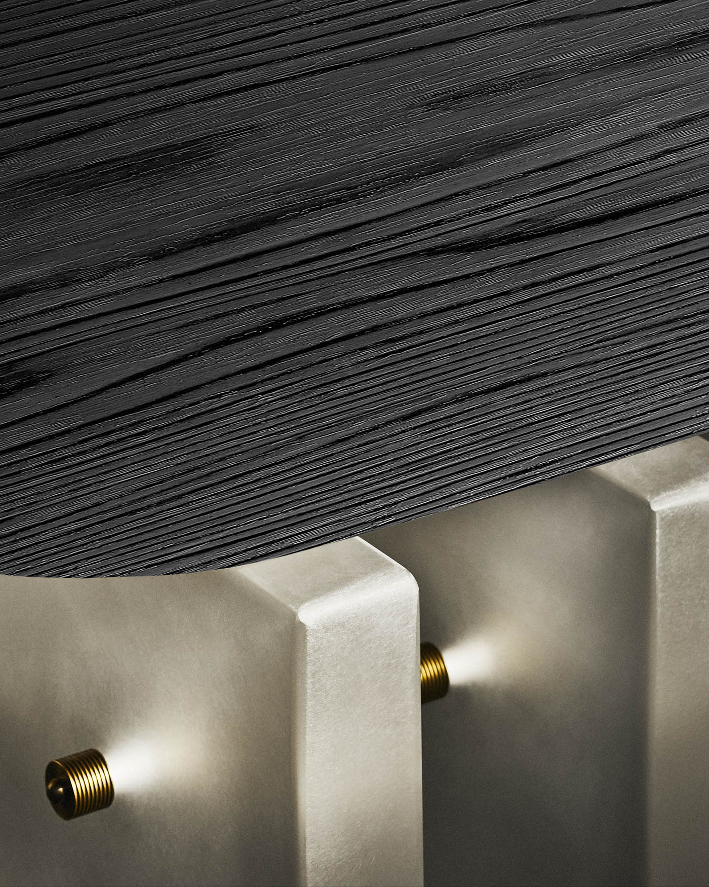 Close-up of black textured wooden coffee table top resting on smooth beige concrete block supports with brass bolts