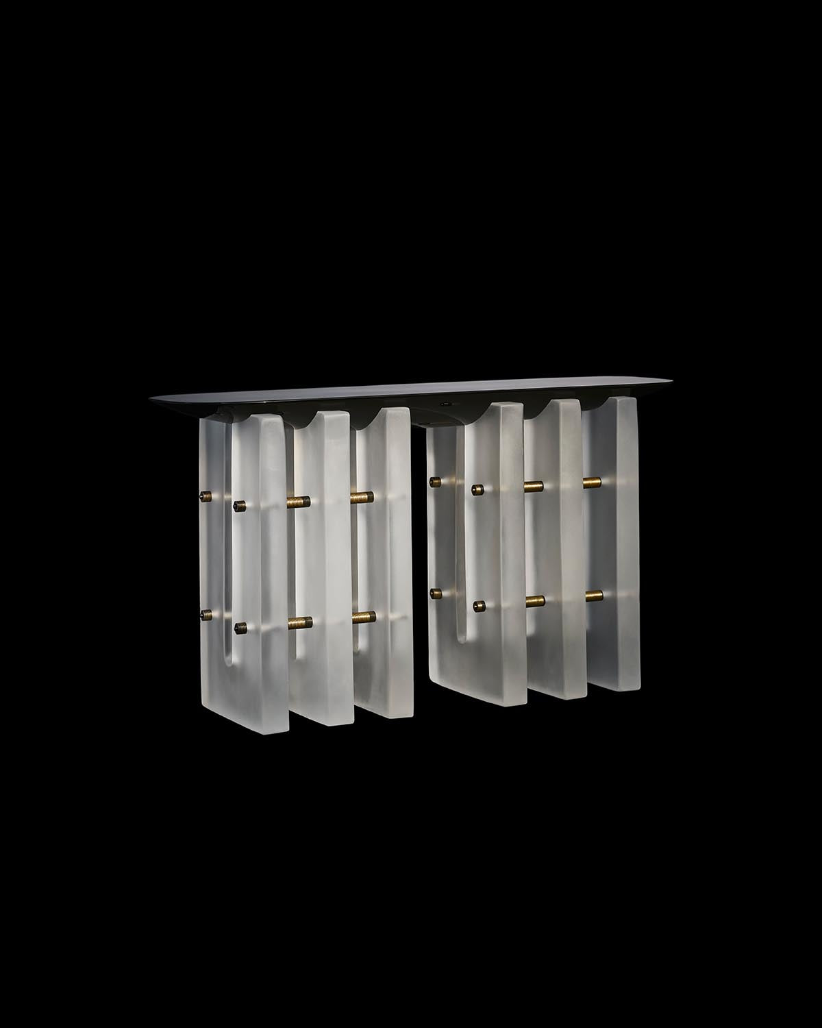 Console table with frosted glass vertical panels connected by brass rods and a smooth dark tabletop against black background