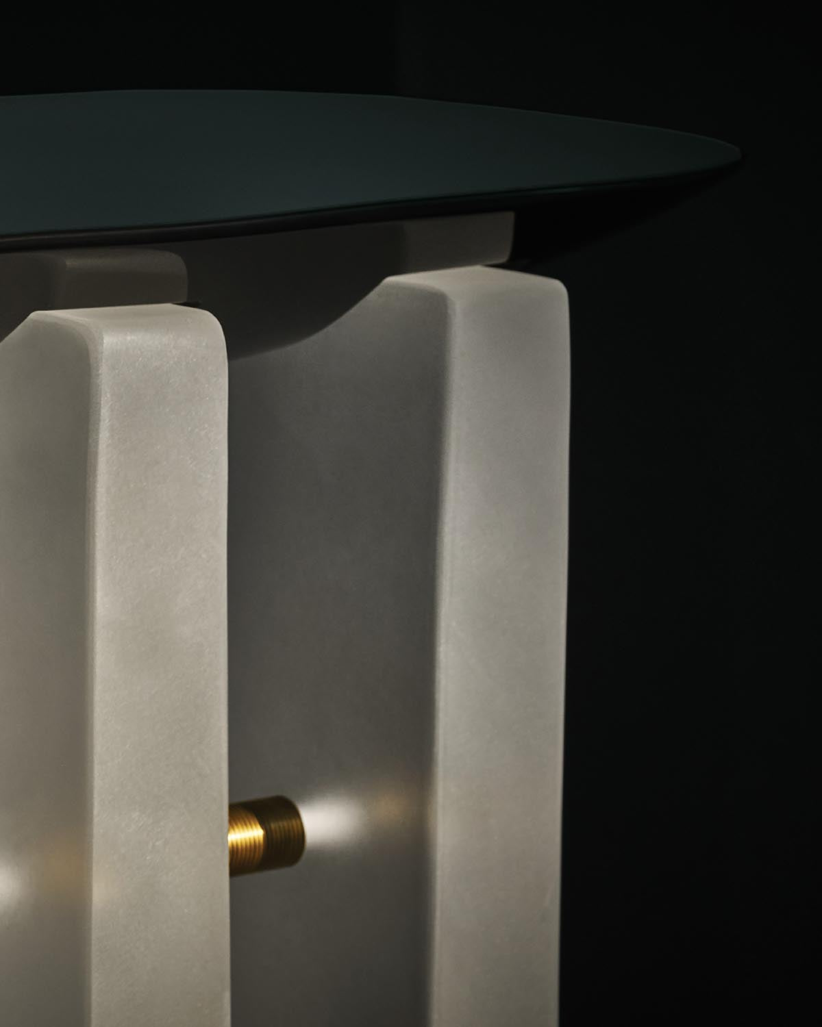 Close-up of a console table featuring smooth white stone vertical supports connected by a brass rod under a dark tabletop against black background