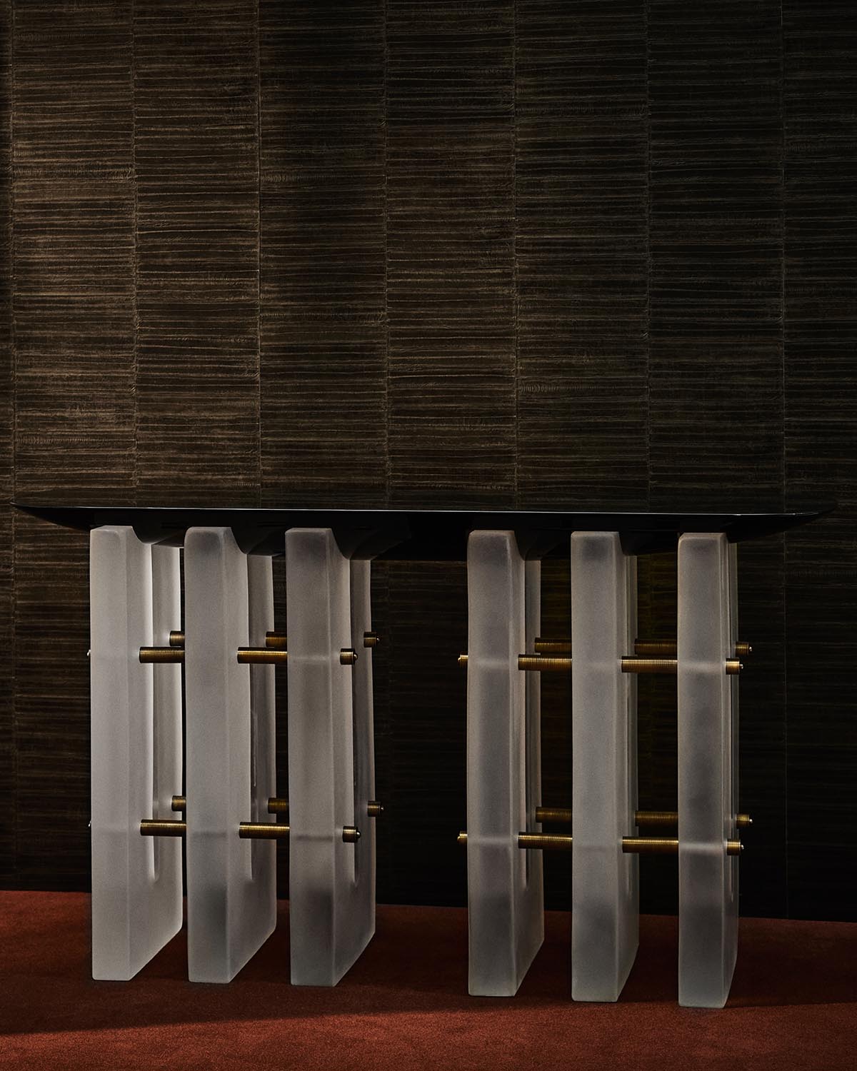 Modern console table with frosted vertical glass panels connected by horizontal brass rods and a dark rectangular top