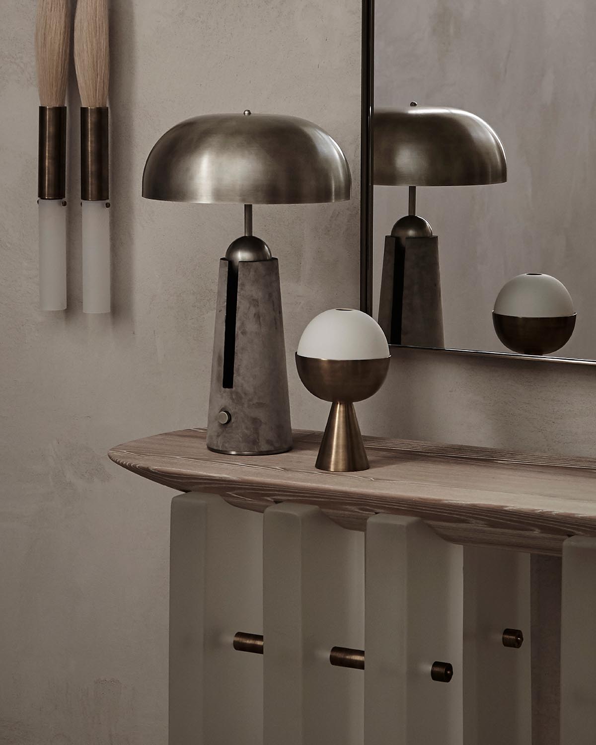 Minimalist wooden console table with metallic dome lamp and decorative orb sculpture against textured wall and mirror