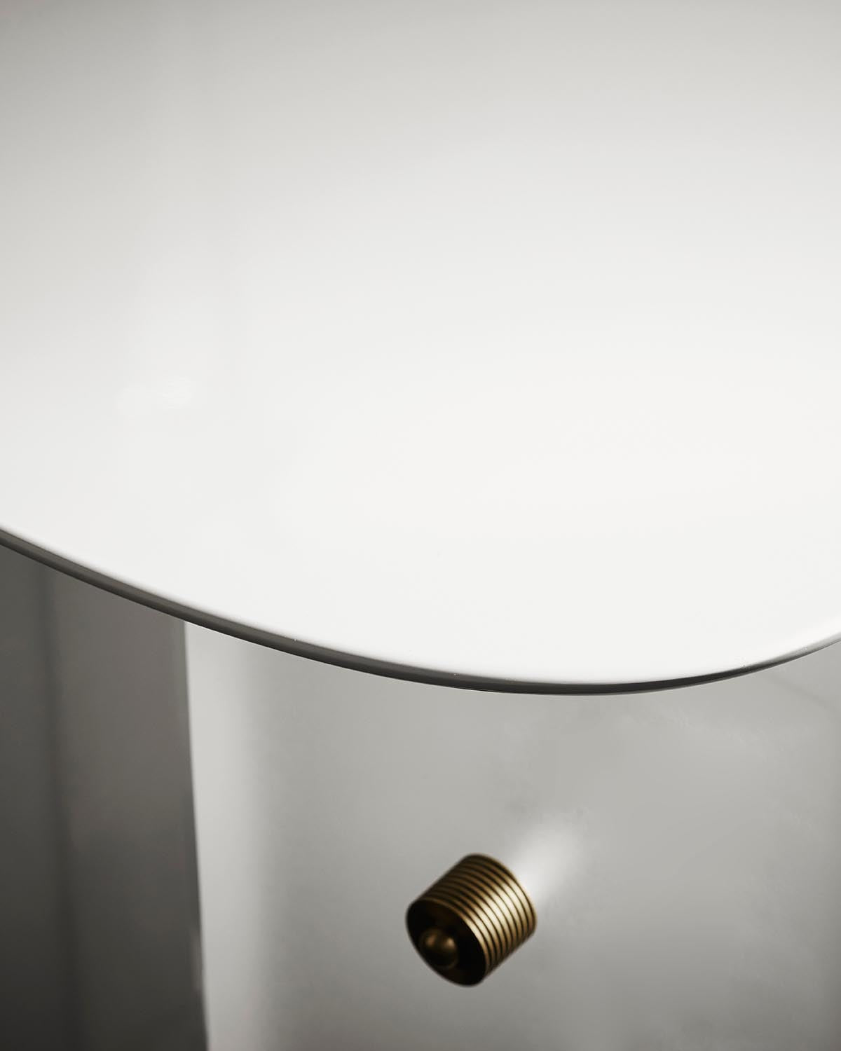 Close-up of white curved dining table edge with brass ribbed knob detail against a light background