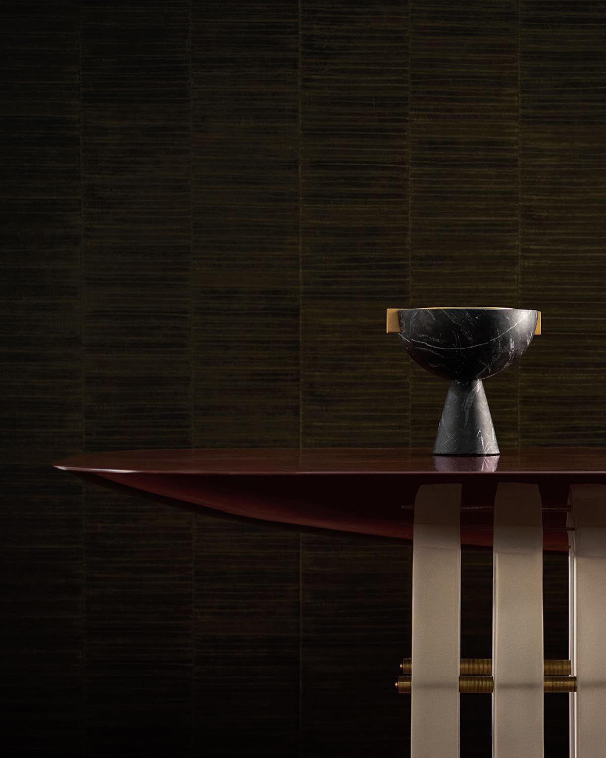 Close-up of a dark wooden dining table with sculptural black stone bowl and brass accents against textured dark wall