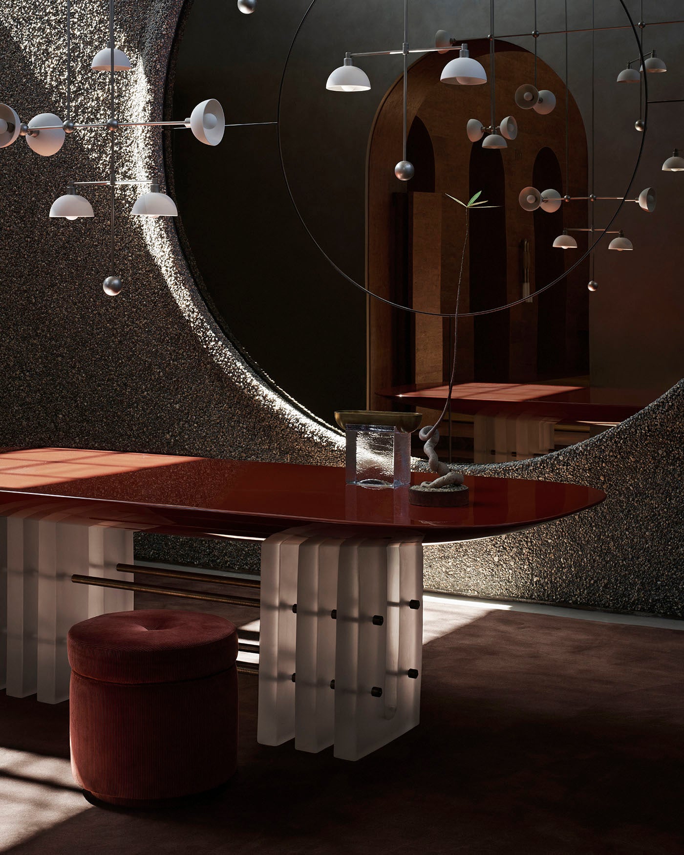 Glossy red dining table with translucent pedestal base, round velvet stool, and modern pendant lighting in textured interior space