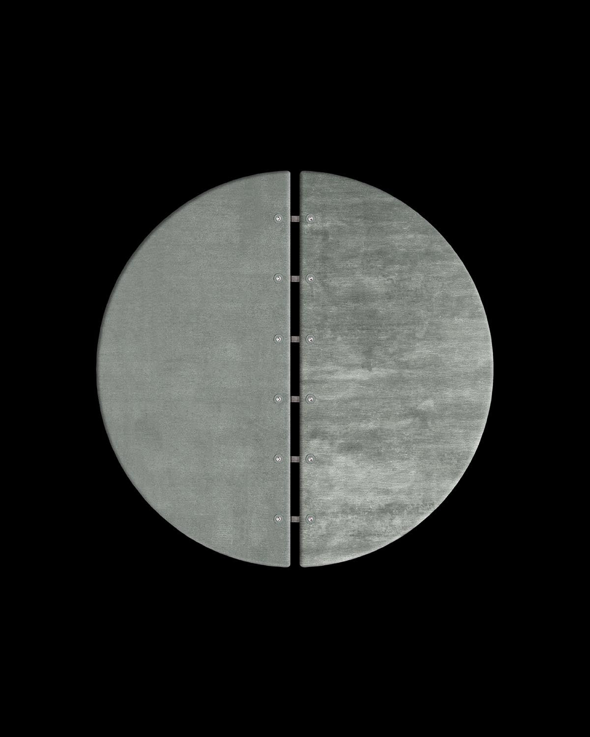 Top-down view of a round rug split in half, with small metal connectors along the center gap on a black background