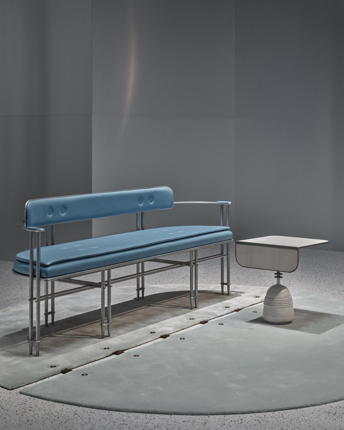 Modern seating bench with blue cushioned seat and backrest paired with a minimalist sculptural side table on gray rug