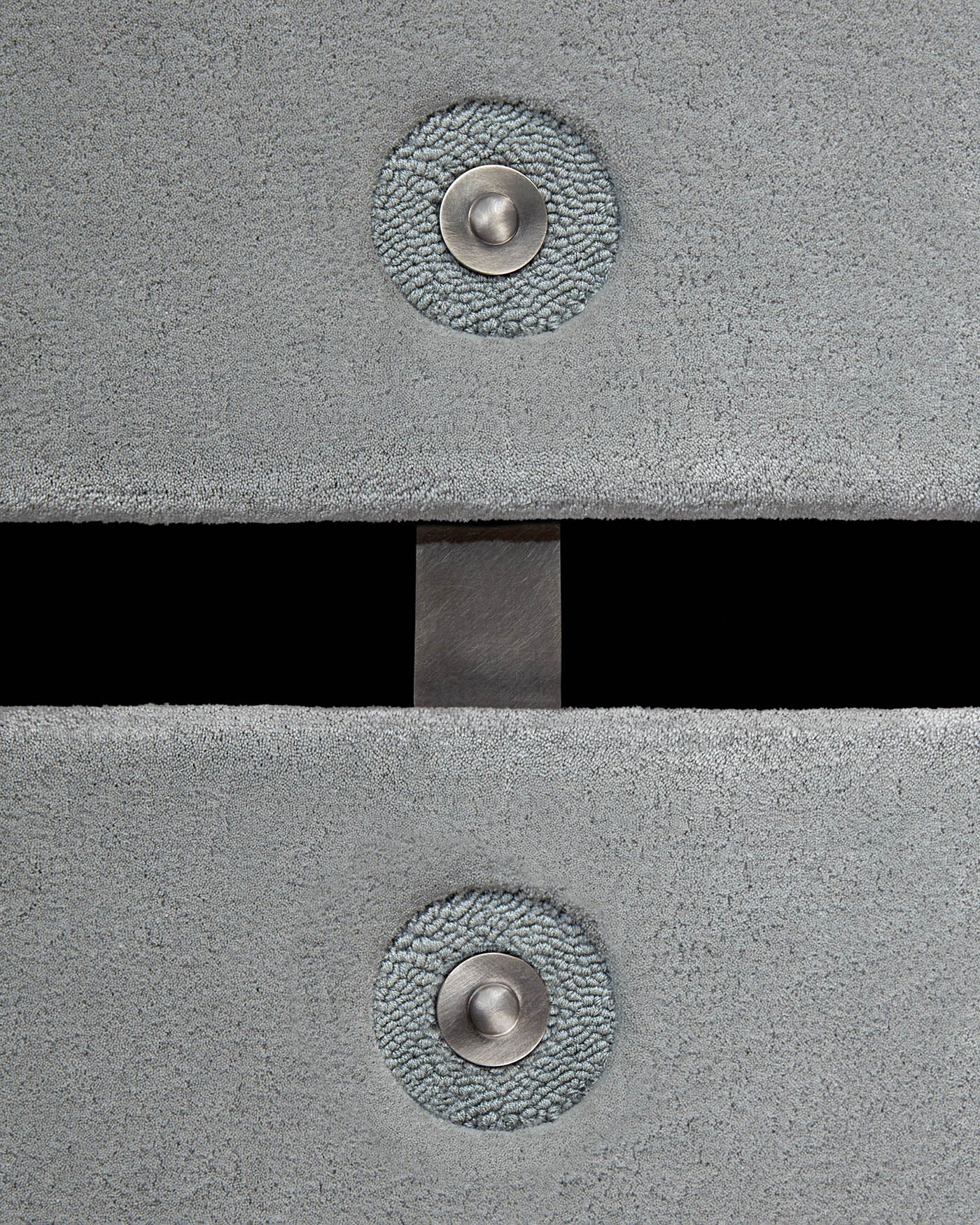 Close-up of two textured gray carpets with metal circular fasteners and a dark rectangular gap in between against black background