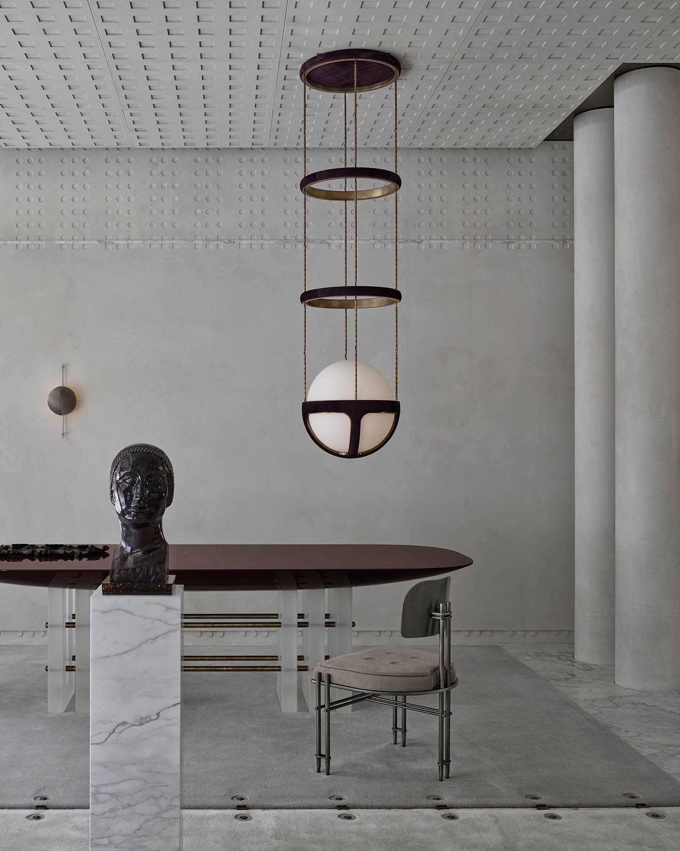 Minimalist interior with a sculptural black bust on a marble pedestal, dark oval table, pendant light, and textured grey walls