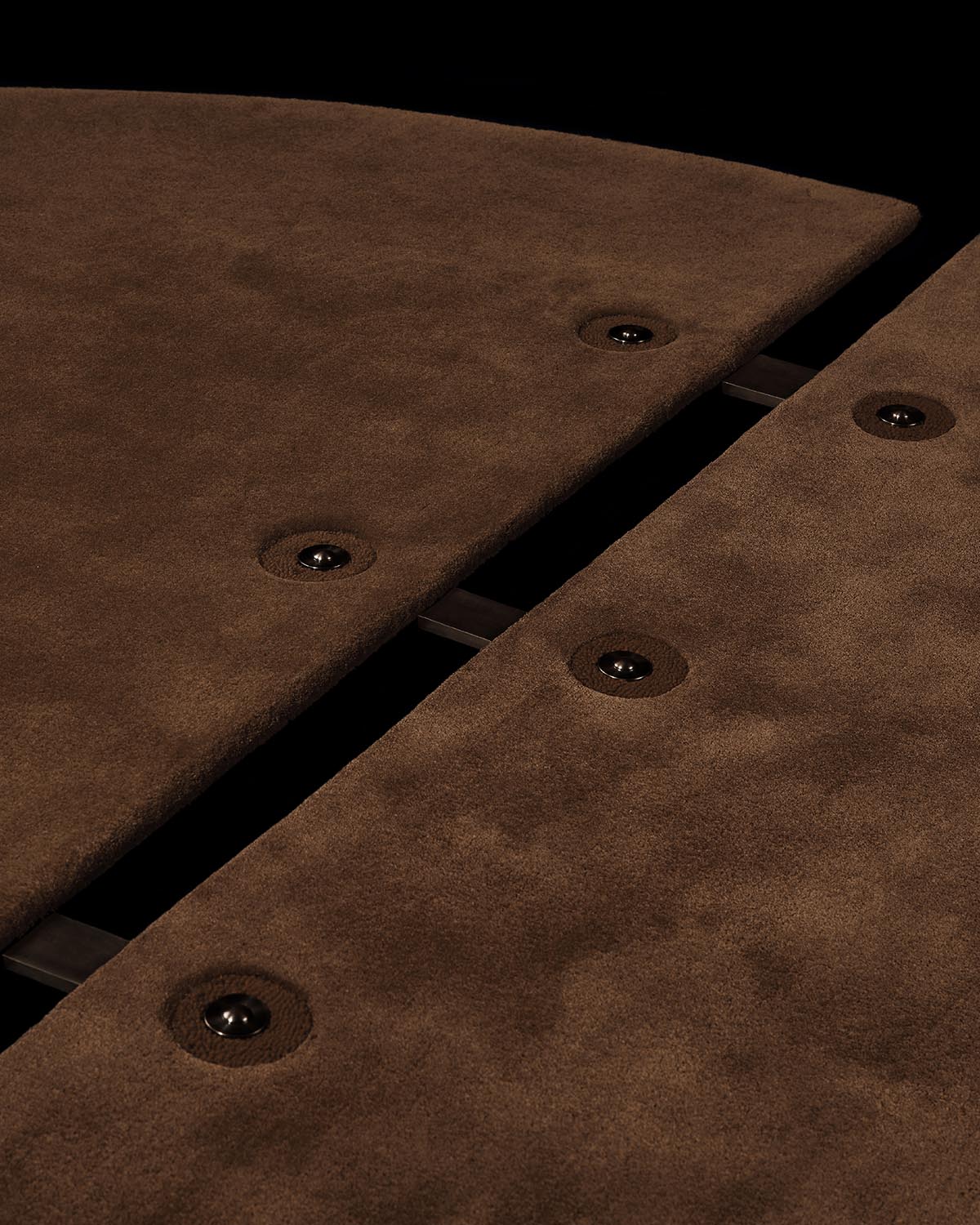 Close-up of dark brown rug panels with black button accents and visible metal connecting rods on a black background