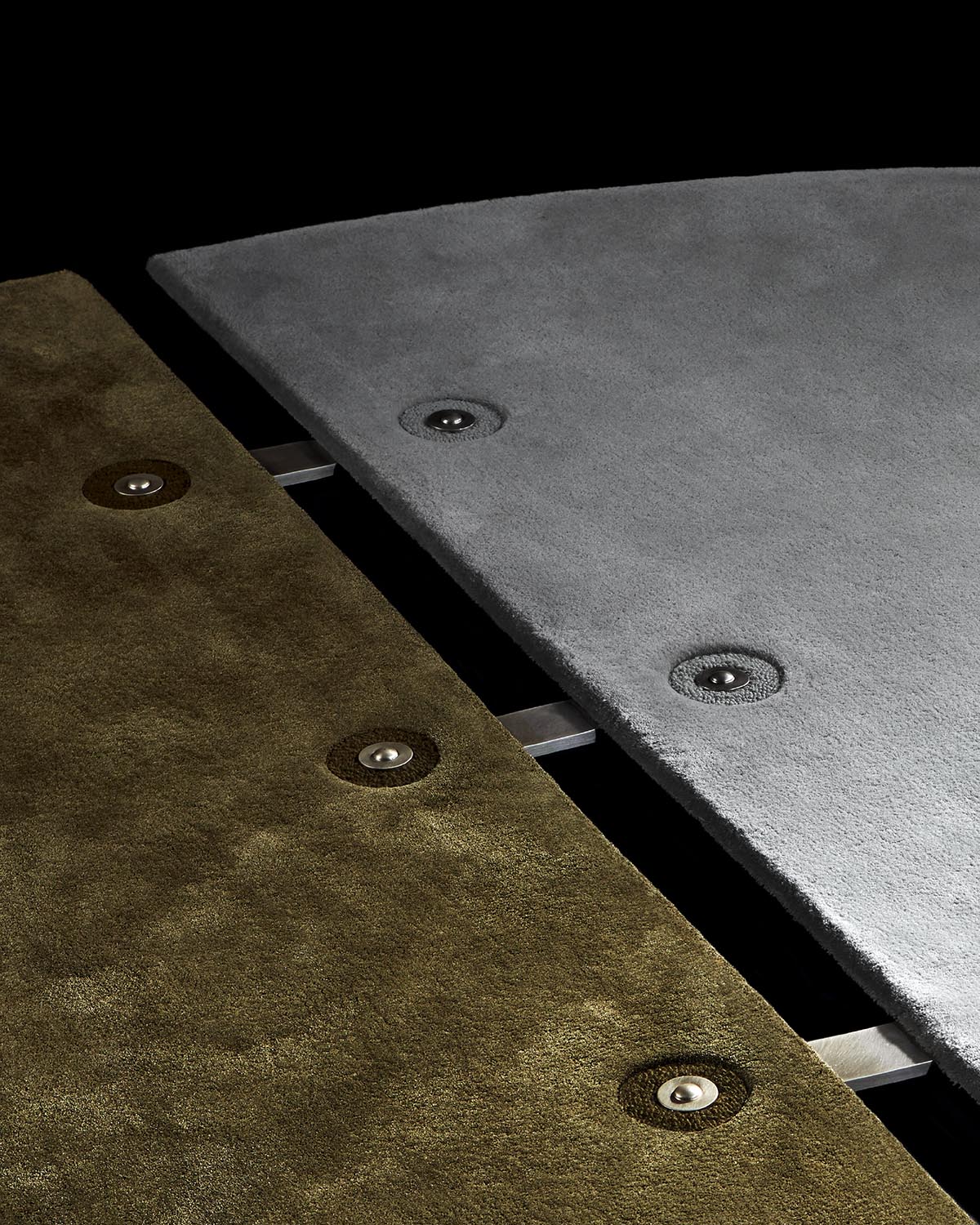 Close-up of two triangular carpet panels in olive green and gray with metal connectors on a black background