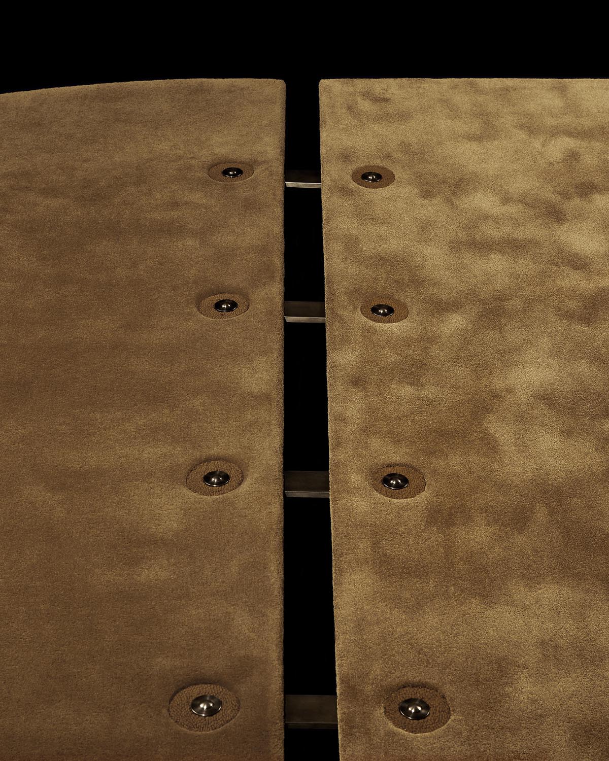 Close-up of two textured brown carpet panels with evenly spaced buttons and metal connectors on a black background