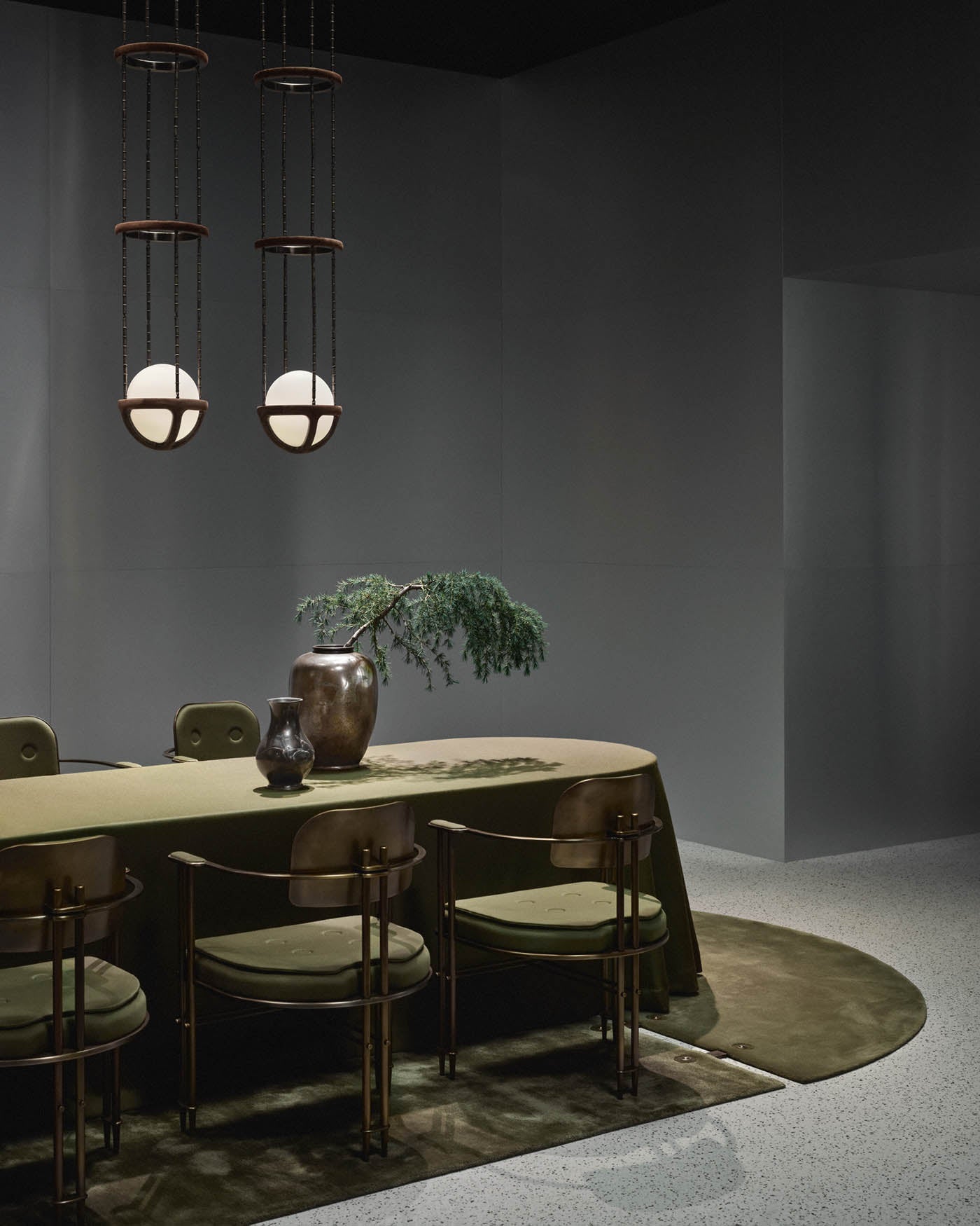 Minimalist dining room with olive green velvet tablecloth, matching chairs, ceramic vases, and two spherical pendant lights