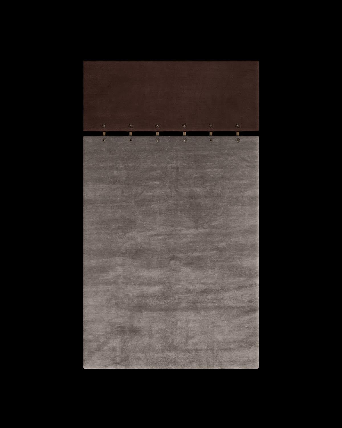 Top view of a rectangular gray rug with a smaller dark brown panel attached by metal rings against a black background