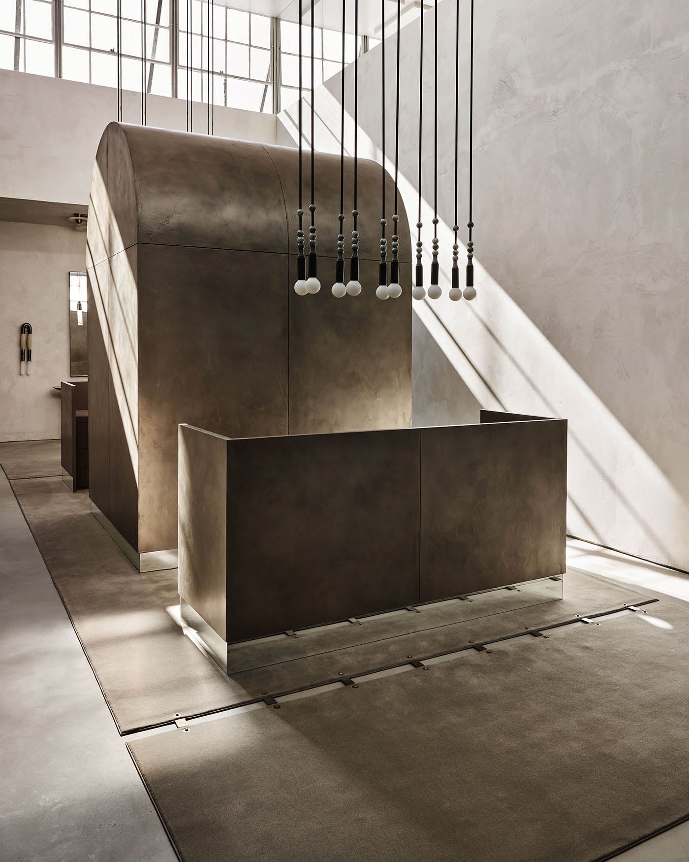 Minimalist interior with large curved concrete structure, rectangular partition, and hanging pendant lights casting shadows on textured walls