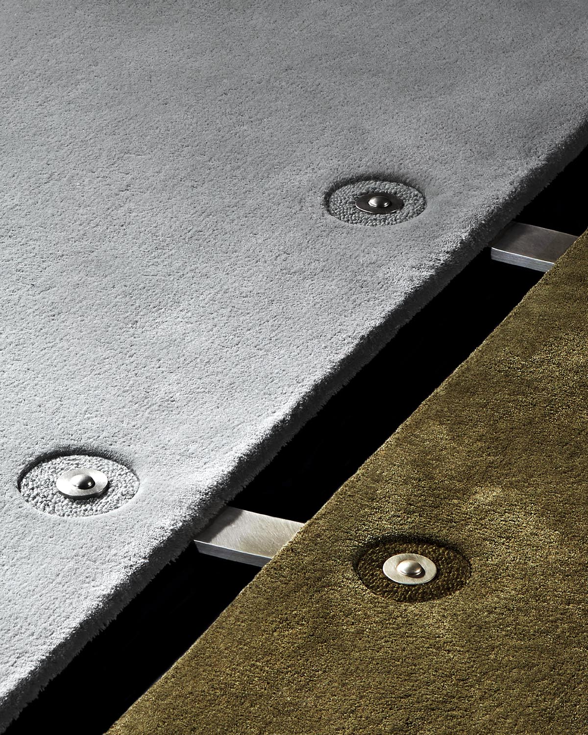 Close-up of overlapping gray and olive textured panels with recessed metal fasteners and brushed metal connectors visible underneath