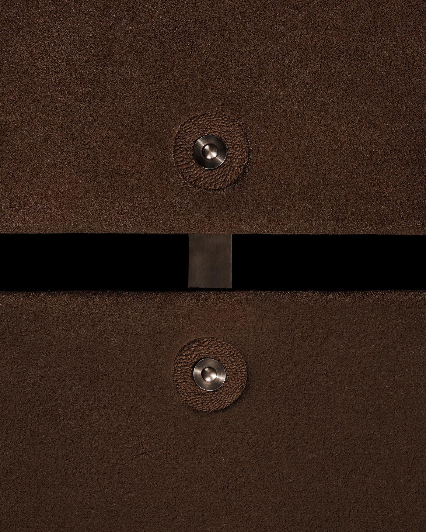 Close-up of a brown textured surface with two round metal buttons and a narrow horizontal gap in the center against a dark background