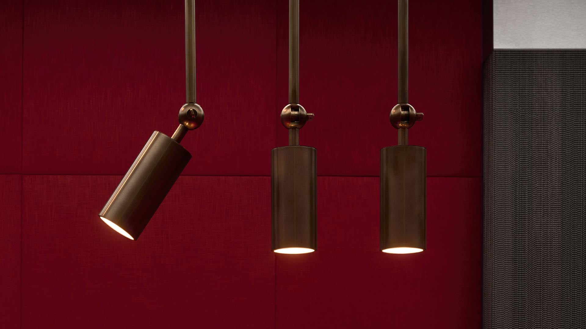 Three cylindrical bronze pendant lights hanging against a dark red textured wall background