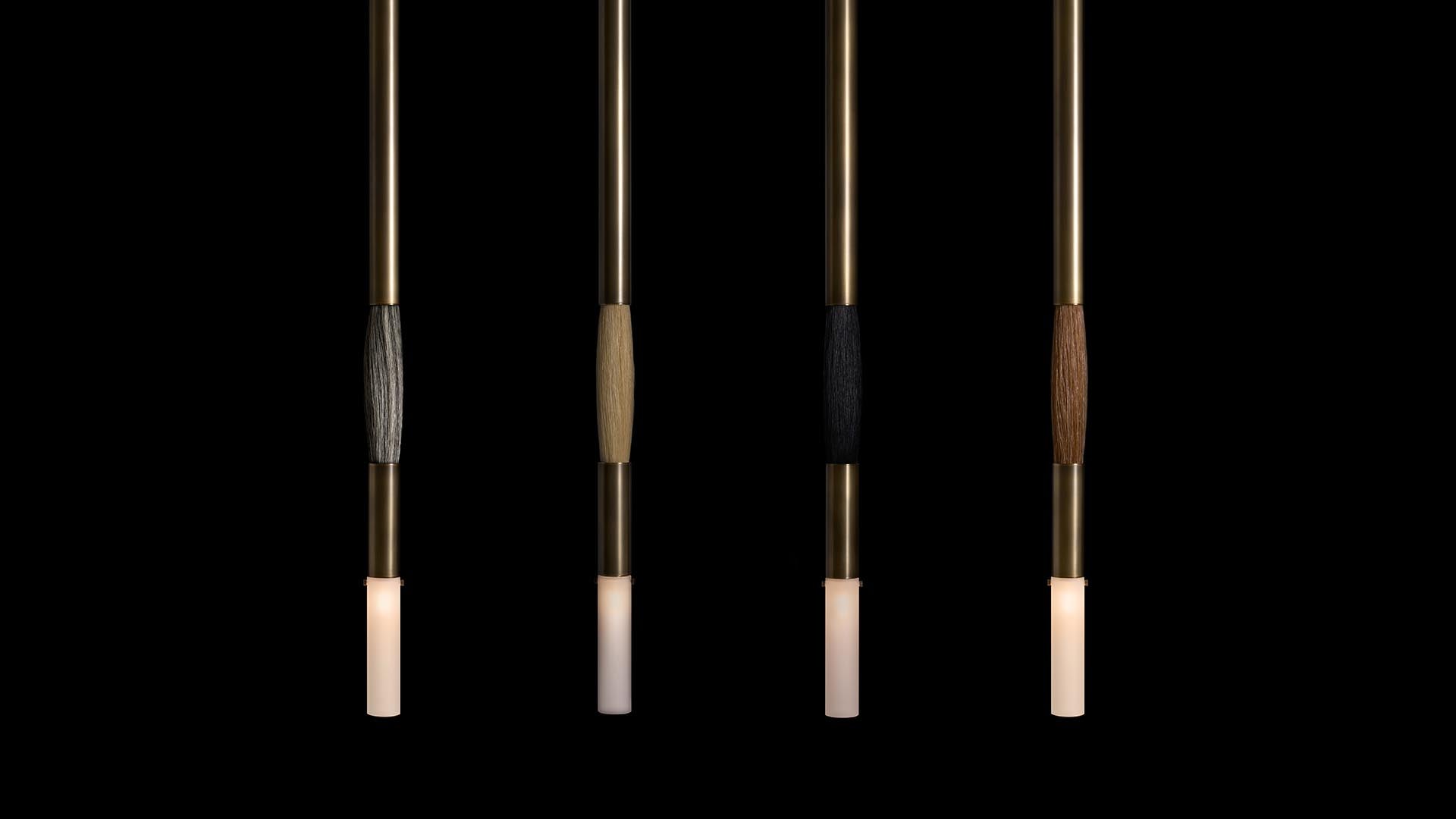 Four vertical pendant lights with cylindrical frosted glass shades and textured wooden accents on brass rods against a black background