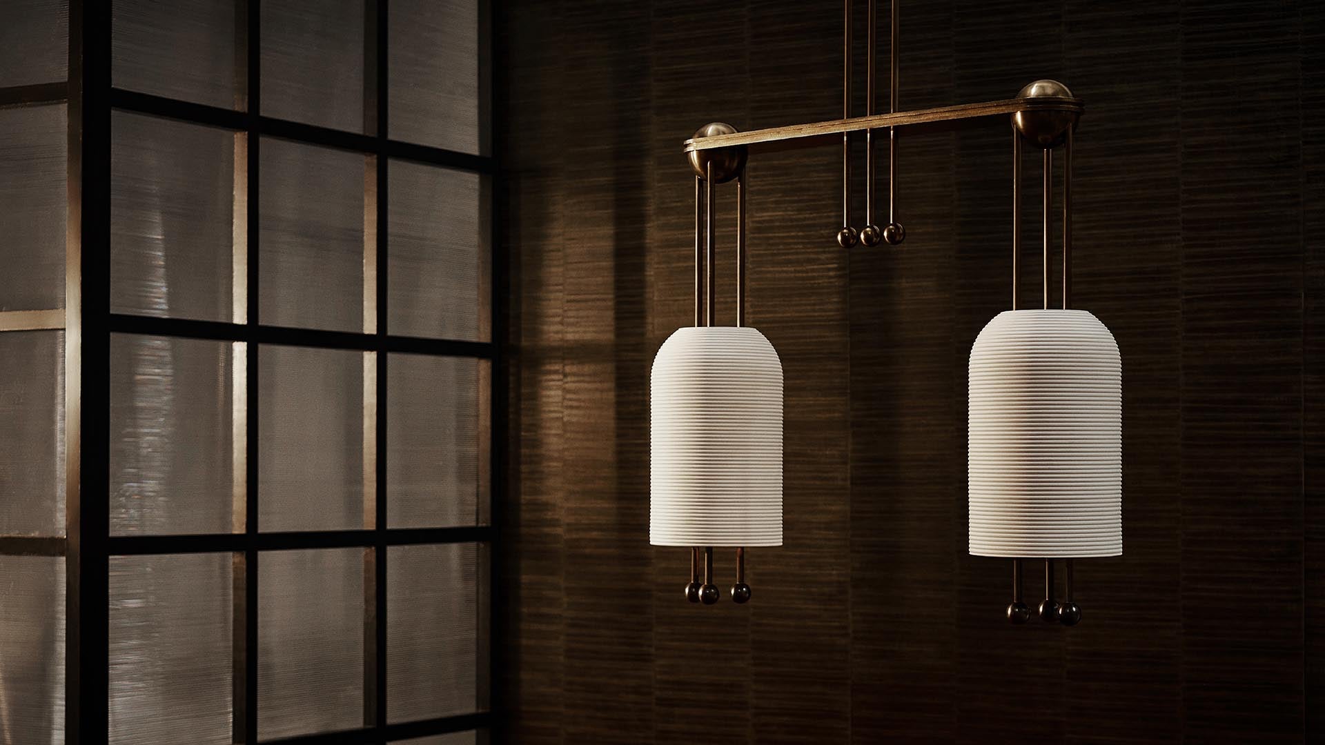 Minimalist double pendant light with ribbed white shades hanging against a textured dark brown wall and a black-framed window panel