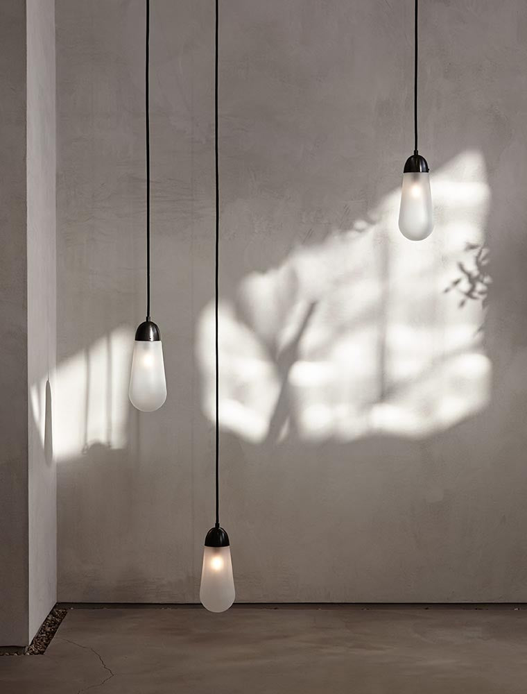Three elongated frosted pendant lights hanging at different heights against a textured beige wall with shadow patterns