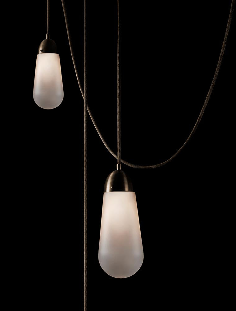 Two elongated frosted glass pendant lights with dark metal fixtures suspended by black cords against a black background
