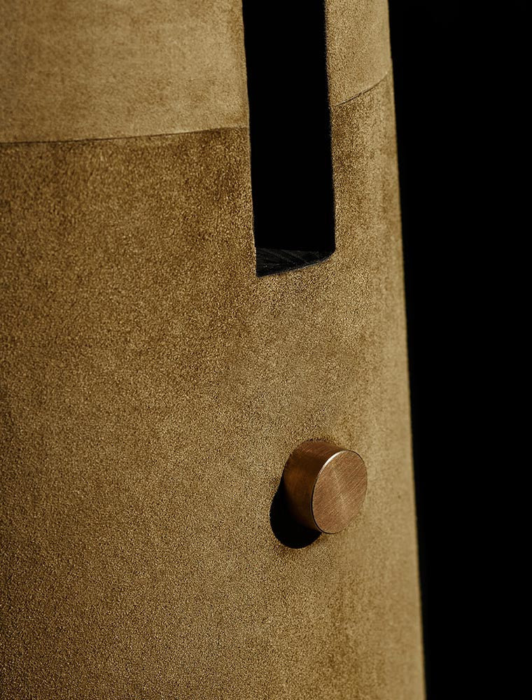 Close-up of a textured brown suede surface with a vertical black slit and round metallic knob against a black background