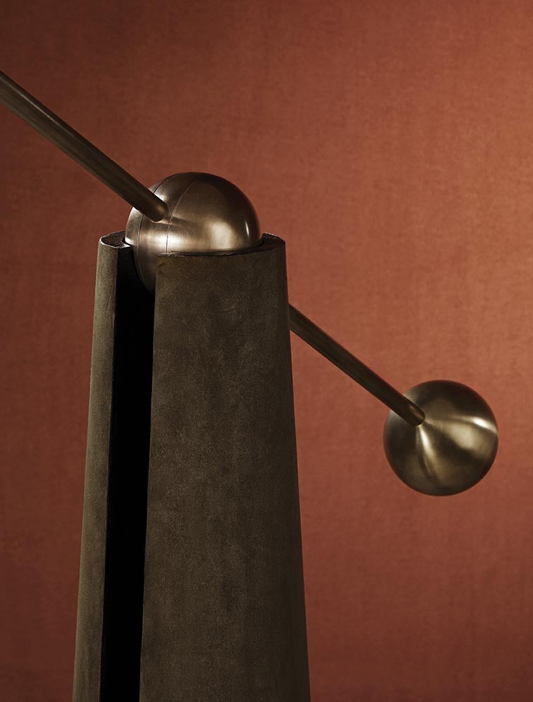 Close-up of a dark textured vertical sculpture with intersecting bronze spheres and rods against a warm brown background